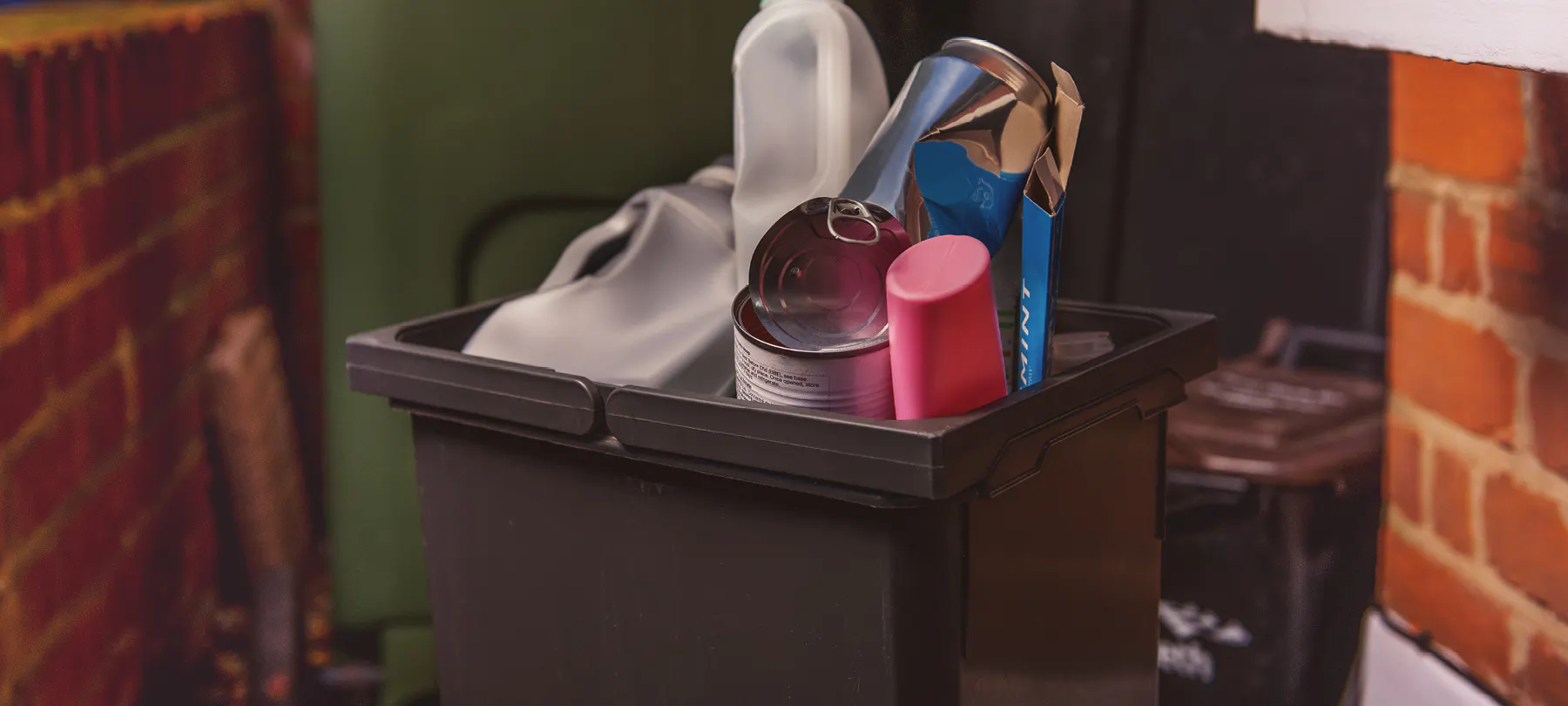 Open brown plastic recycling container showing recycable materials inside on a doorstep