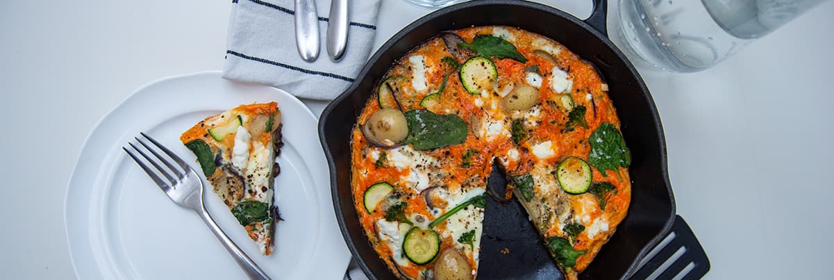Vegetable omelette in a pan with a portion taken out and served on a white plate